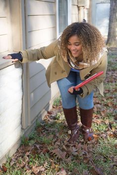 a woman leaning on the side of a house while holding onto a red umbrella and wearing boots