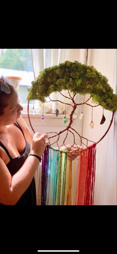 a woman is making a tree decoration out of yarn and beads on a window sill