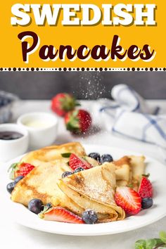 pancakes with strawberries and blueberries are on a white plate next to some fruit