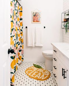 a white bathroom with yellow and black decor on the shower curtain, toilet seat cover and rug