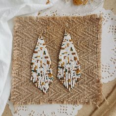 two pairs of white beaded earrings sitting on top of a piece of burlock