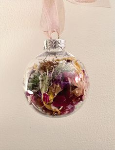 a glass ball ornament with dried flowers in it hanging from a pink ribbon