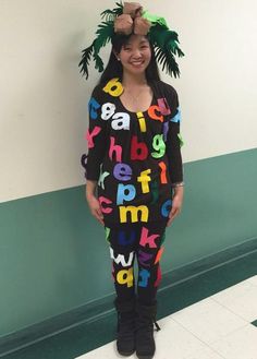 a woman standing in front of a wall wearing a black and multicolored sweater with letters on it