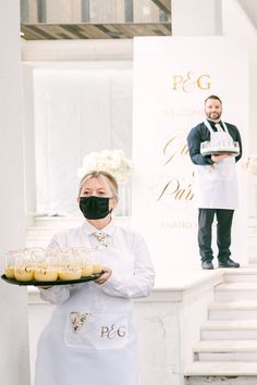 a woman wearing a face mask holding a tray of food in front of a man