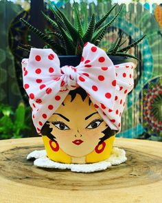 a potted plant with a red and white bow on it's head sitting on top of a wooden table