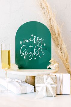 a green sign that says merry and bright next to some presents on a white table