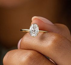 a woman's hand holding a diamond ring in her left hand, with the center stone on top