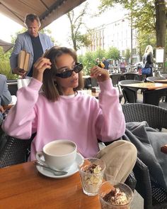 a woman sitting at a table in front of a cup of coffee and an ice cream sundae