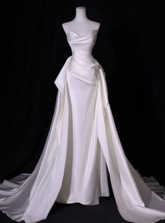 Held with an aura of sculptural elegance, this wedding dress is a masterpiece of fabric artistry. The bodice, a dramatic play of wrapped satin, is both structured and fluid, leading the eye to a slender waist before unfolding into a luxurious full skirt and train. The off-shoulder neckline is a portrait of modern grace, offering a canvas for an exquisite necklace or the natural beauty of the bride's radiance. This gown is the embodiment of a bride's singular moment, a garment designed to echo the unique joy of a wedding day. Silhouette:mermaidHemline:floor lengthNeckline:straplessFabric:satinShown Color:whiteSleeve Style:sleevelessBack Style:lace upEmbellishment:pleatsBuilt-in Bra: yes Satin Wedding Dress With Ruching, Afterparty Wedding Dress Long, Fitted Satin Wedding Dress With Train, Wedding Dresses Halter Top Neckline, Mermaid Silhouette Wedding Dress, Unique Simple Wedding Dresses, Flowy Elegant Wedding Dress, Wedding Dresses Ranch Style, Kim Casas Wedding Dress