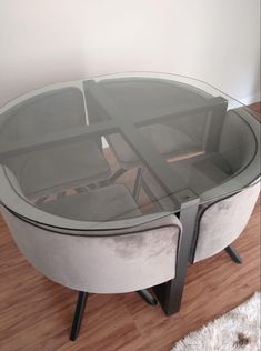 a round glass table with metal legs on wooden flooring in front of a white wall