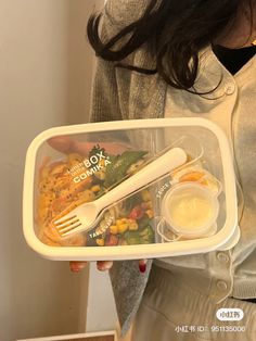 a woman holding a plastic container with food in it and utensils in it