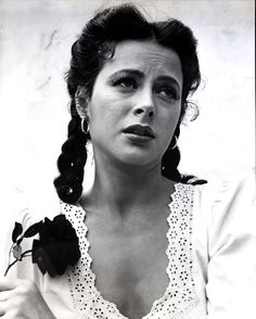 an old black and white photo of a woman with a flower in her hair, looking at the camera