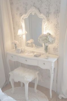 a white dressing table with a mirror, stool and flowers in vases on it