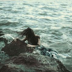 a woman sitting on top of a rock in the ocean