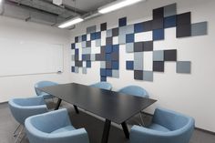 an empty conference room with blue chairs and a black table in front of a wall that has squares on it