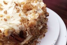 a piece of cake with white frosting and pecans on top sitting on a plate