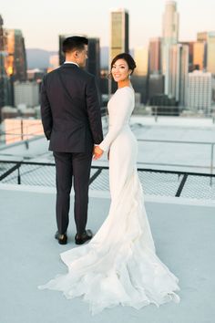 a bride and groom holding hands on top of a roof in front of the city skyline