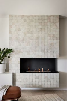 a modern fireplace in a living room with white tiles on the wall and a potted plant next to it