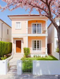 a house with pink flowers on the trees in front of it and a white fence