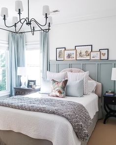 a white bed sitting under a chandelier in a bedroom next to a window