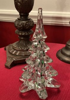 a glass christmas tree sitting on top of a red tablecloth covered table next to two metal candlesticks