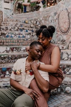 a man and woman sitting on top of each other in front of a mosaic wall