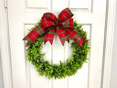 a green wreath with red and green plaid bow hanging on a white door