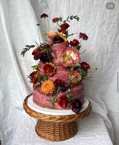 a three tiered cake with flowers on top sitting on a wicker platter