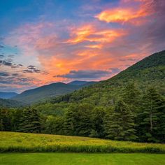 the sun is setting in the mountains with green grass and trees on either side of it