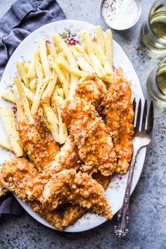 chicken tenders and french fries on a plate with two glasses of wine in the background