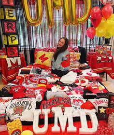 a woman sitting on top of a bed surrounded by red and yellow balloons in the shape of letters