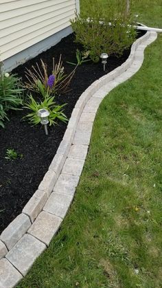 a small garden with flowers and plants in the grass next to a home's front yard