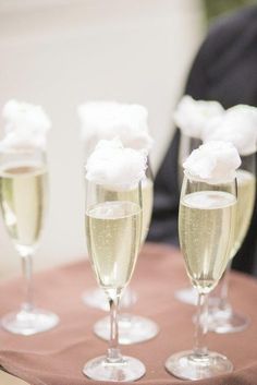 three champagne flutes are sitting on a table with white flowers in the middle and one is filled with bubbles