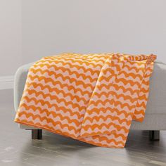 an orange and white blanket sitting on top of a couch next to a gray chair