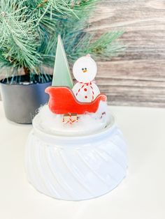 a snowman sitting on top of a sleigh next to a christmas tree