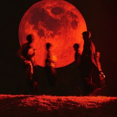 several people walking in front of a large red moon with the silhouettes of two men