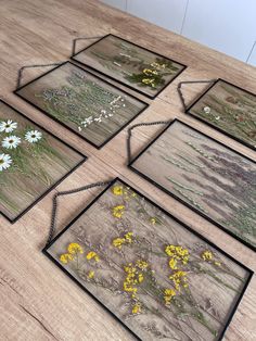 four framed pictures with wildflowers and grass in them on a wooden table top