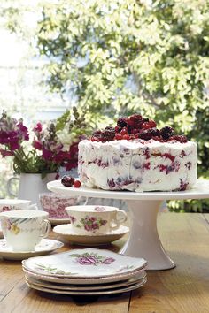 a cake sitting on top of a table next to cups and saucers with flowers in the background