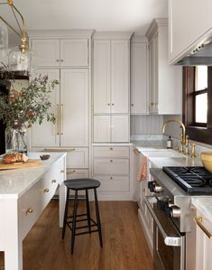 a kitchen with white cabinets and wood flooring has a stool next to the stove