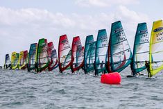 a row of windsurfers in the water with their sails down and red buoy