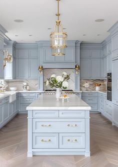 a large kitchen with blue cabinets and white counter tops, gold accents on the chandelier