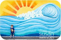 a young boy standing in front of a wall with a mural on it's side