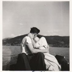 a man holding a baby while sitting on top of a boat next to the ocean