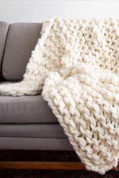 a white knitted blanket sitting on top of a couch