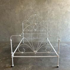 a white metal bed frame with four legs and an intricate design on the headboard