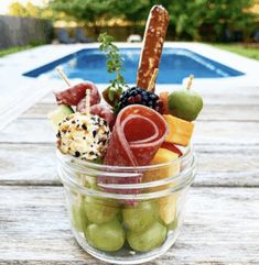 a glass bowl filled with assorted fruits and meats next to a swimming pool