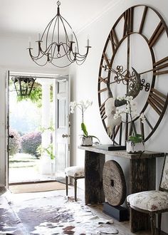 a large clock mounted to the side of a white wall next to a wooden bench