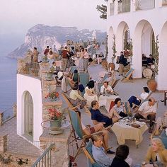 a group of people sitting at tables on the side of a cliff overlooking the ocean