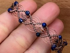 a hand holding a wire wrapped bracelet with blue beads