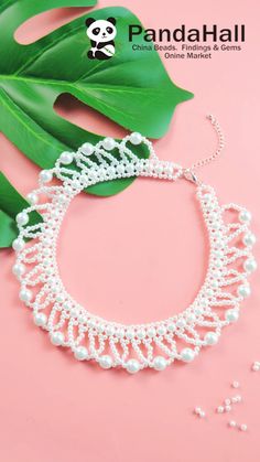 a white bracelet with pearls on it next to a green leaf and some other items